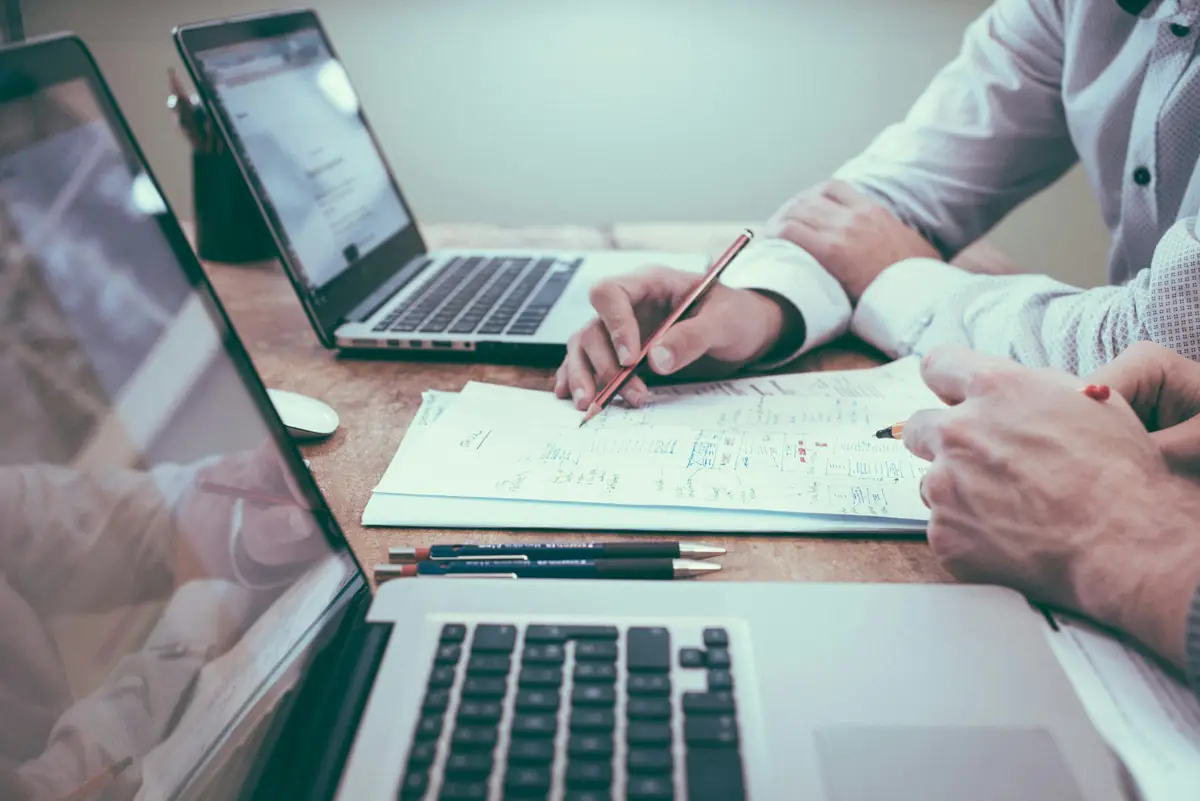 Two people working through printed notes beside their laptops